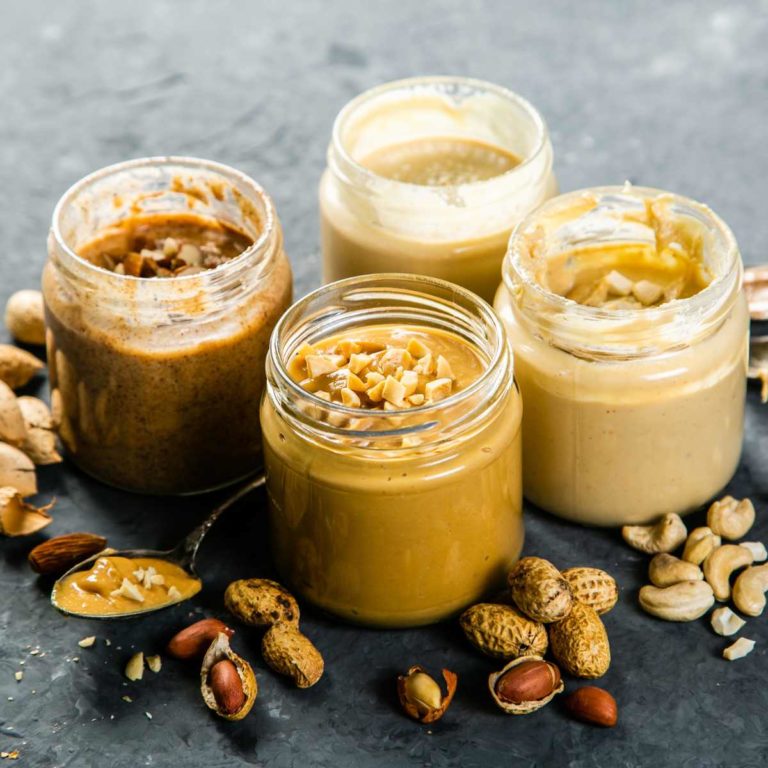 4 jars of different coloured nut butters with scattered nuts