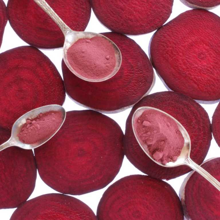 Beetroot powder in spoons over slices of bright purple red beetroot slices