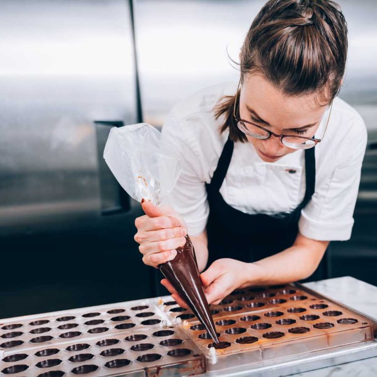Woman filling moulds by piping in dark chocolate